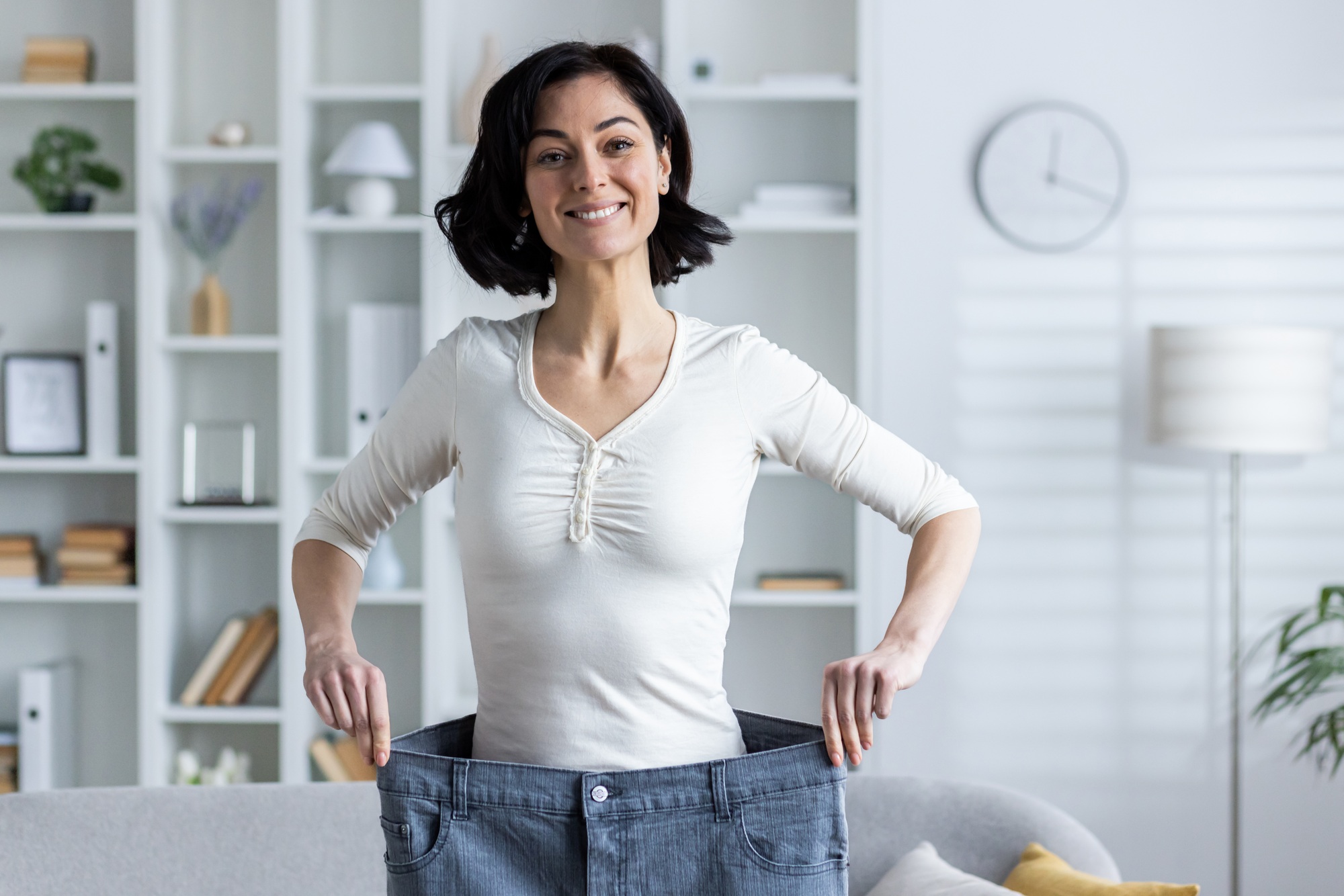 Portrait of a young smiling woman standing at home and showing the result of dieting and losing